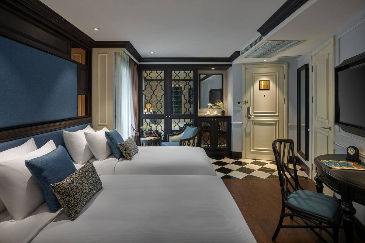 A hotel room with two beds, a desk, a chair, and a television.