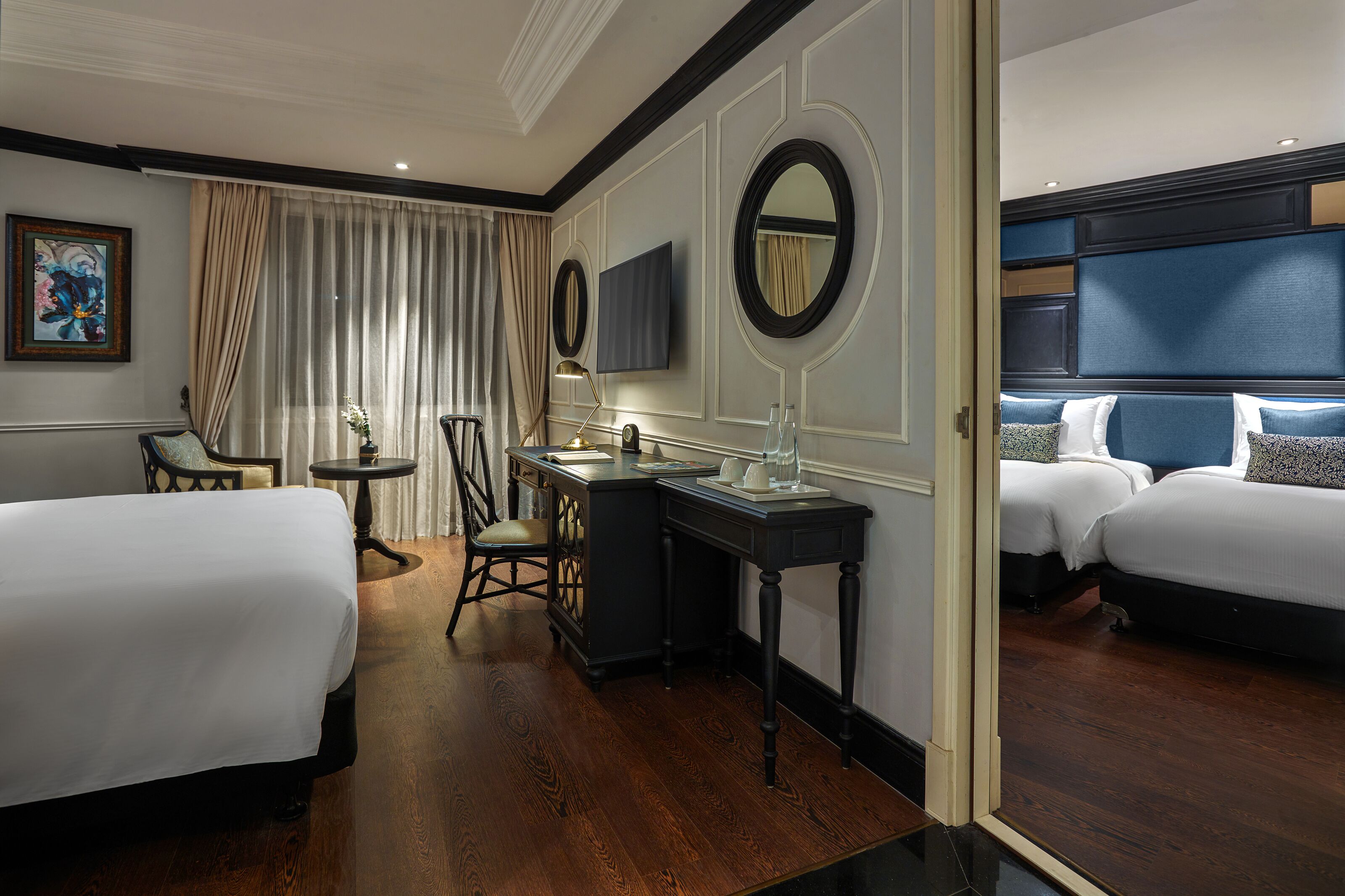 Une chambre d’hôtel avec deux lits, un bureau, une chaise, une télévision et un grand miroir.
