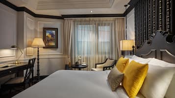 A hotel room with a large bed, two bedside tables, a desk, a chair, and a window with sheer curtains.