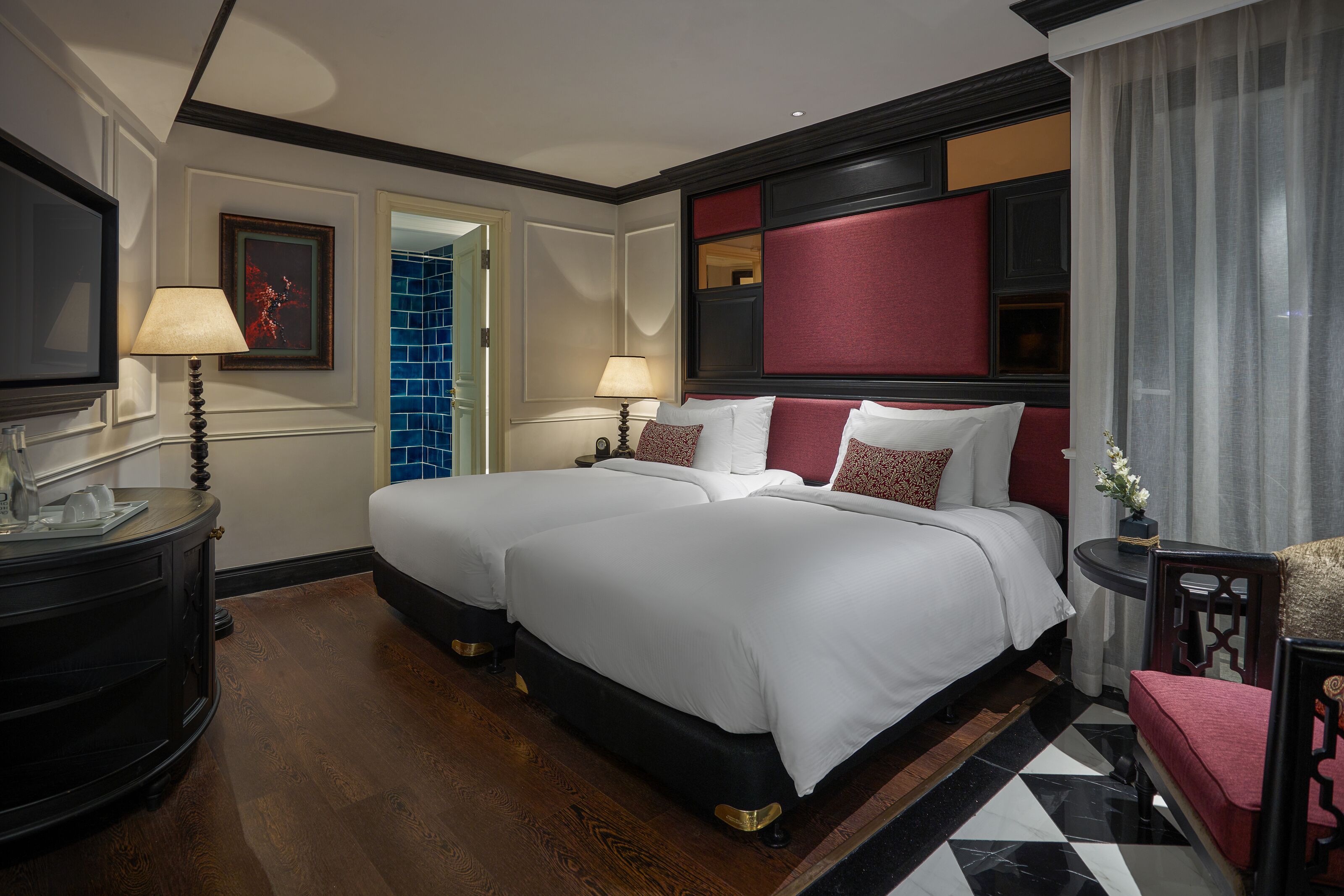 A hotel room with two beds, a TV, a desk with a lamp, and a chair.