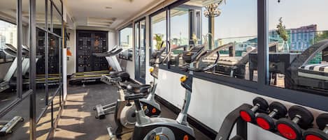 Una palestra con attrezzature per esercizi, ampie finestre e vista sulla città.