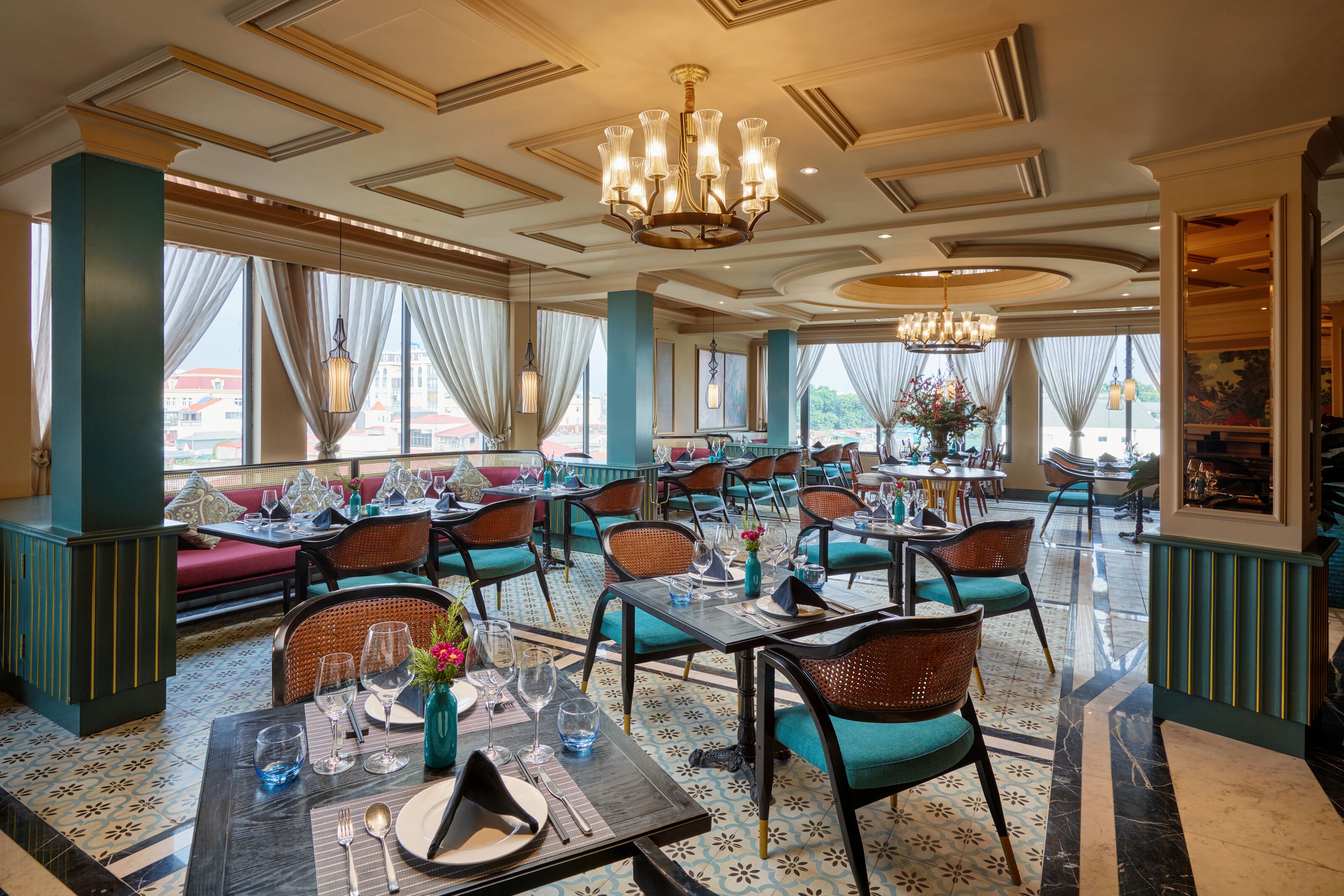 A restaurant with tables and chairs, a chandelier, and large windows with curtains.
