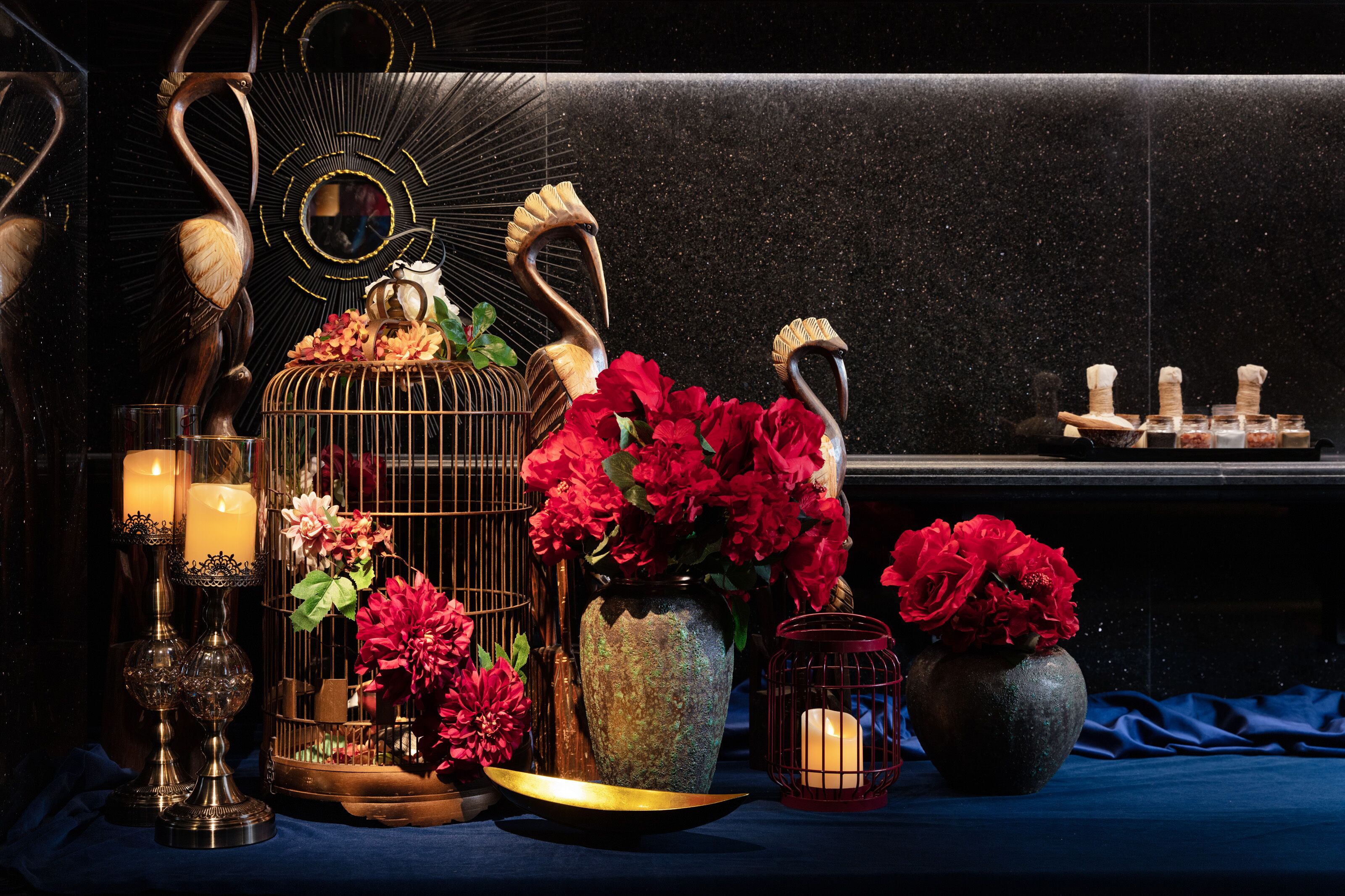 Una mesa con velas, una jaula de pájaros y jarrones de flores.