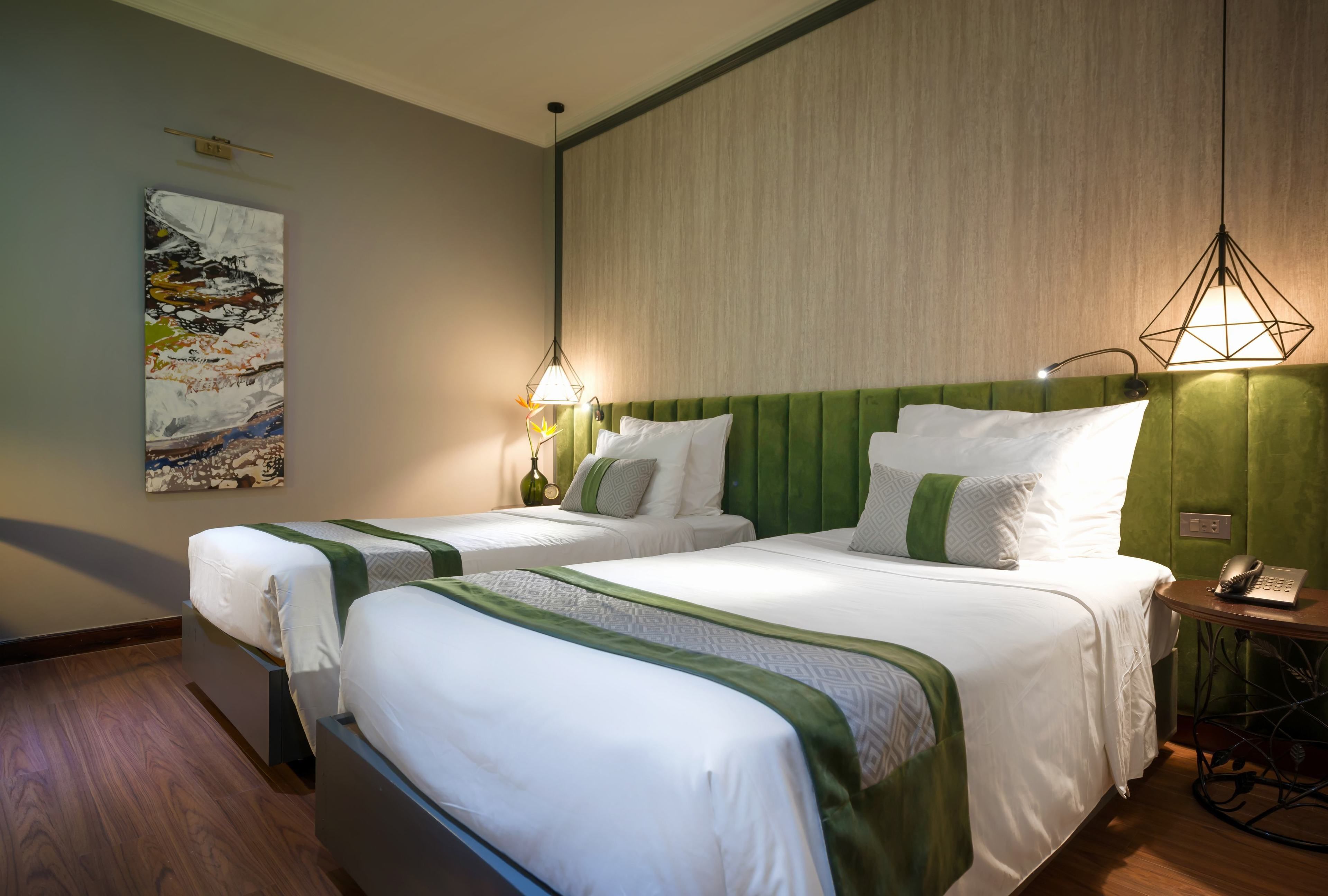 Habitación de hotel con dos camas, cabecera verde, un cuadro en la pared y un teléfono en una mesita de noche.