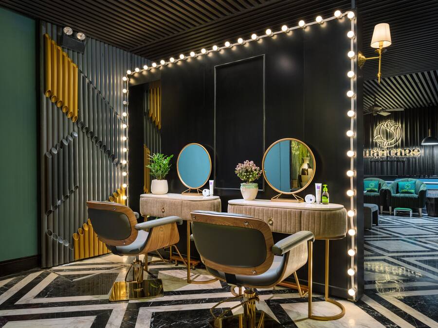 A modern salon with two barber chairs, a vanity with mirrors, and a wall-mounted light fixture.