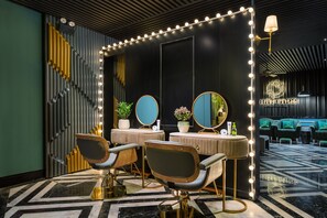 A modern salon with two barber chairs, a vanity with mirrors, and a wall-mounted light fixture.
