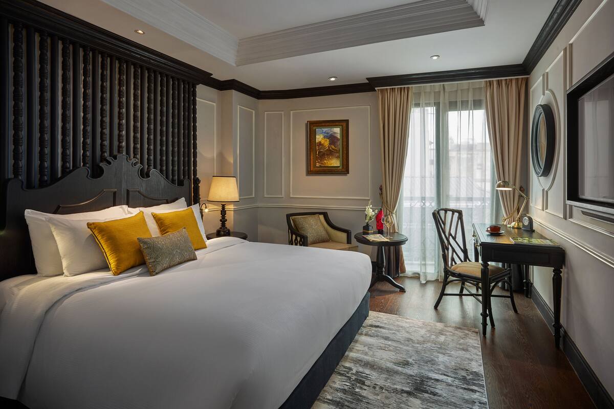 A hotel room with a large bed, a desk, and a chair.