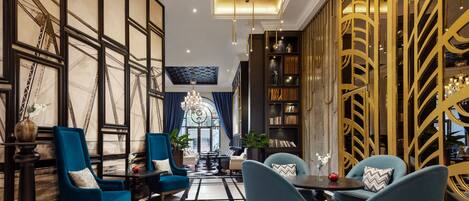 A modern hotel lobby with a black and white tiled floor, blue armchairs, a chandelier, and a gold decorative wall.