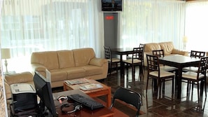 Hotellihuone, jossa on sohva, ruokapöytä tuoleineen, televisio ja työpöytä, jossa on tietokone.