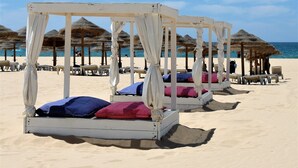 Una playa con camas cubiertas por toldos blancos y sombrillas de paja.