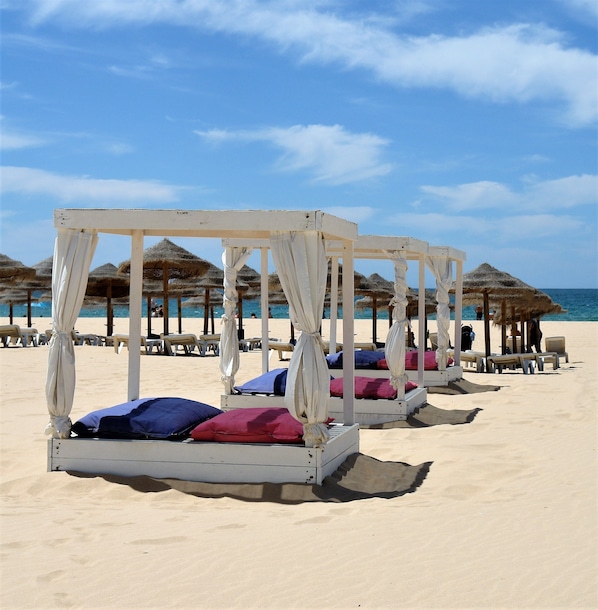A beach with white canopy beds and thatched umbrellas. - Hotel Santa Catarina Algarve (Portimão)