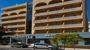 Un hotel de varios pisos con balcones, un restaurante a la vista y un automóvil estacionado adelante.