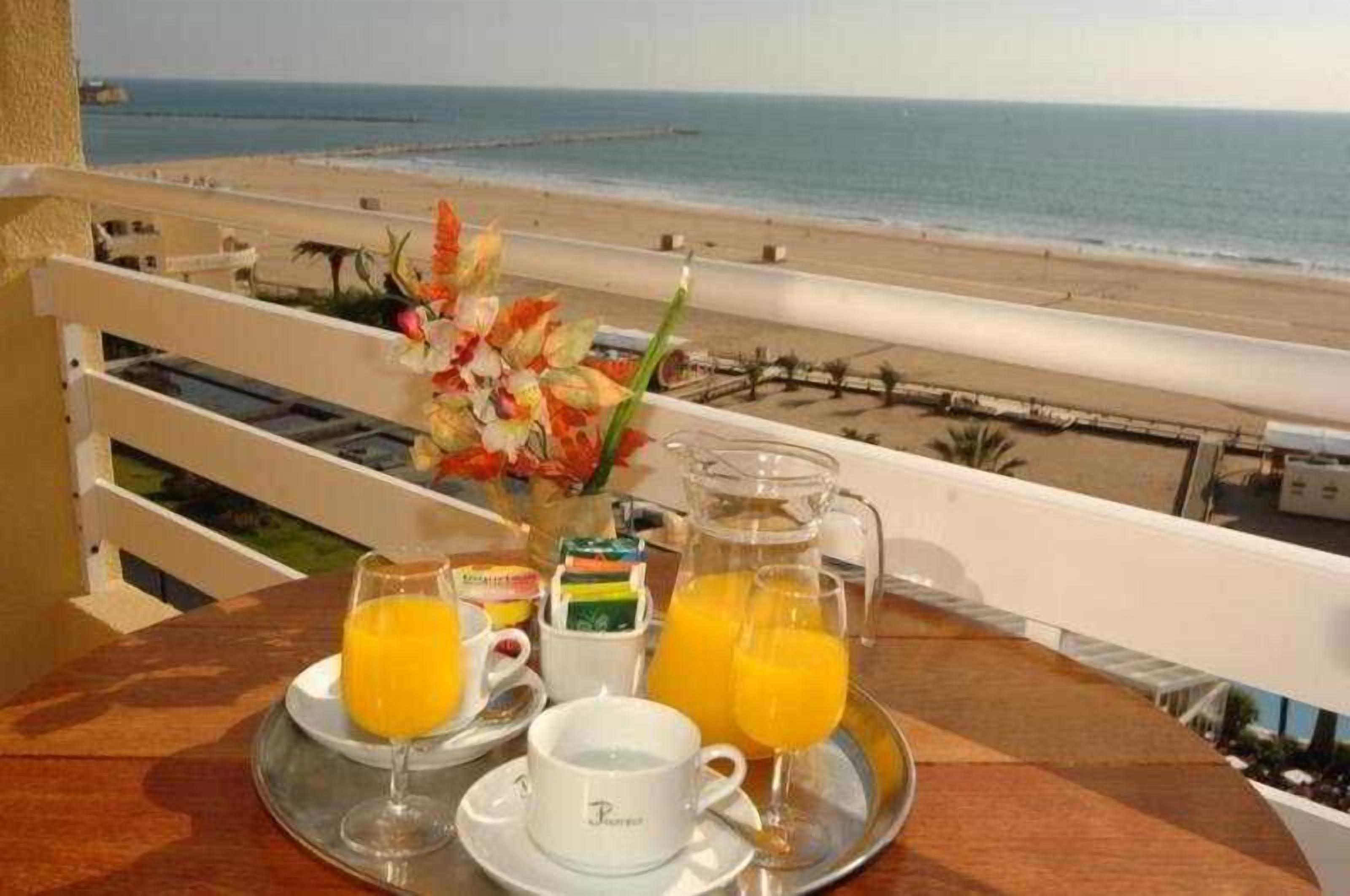 A breakfast setup with orange juice and pastries on a tray, overlooking a beach.