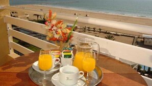 Ontbijt met jus d'orange en gebak op een dienblad, met uitzicht op een strand.