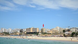 Een kuststadsbeeld met een strand, gebouwen en een rode vlag.