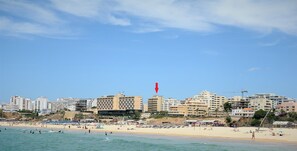 A coastal cityscape with a beach, buildings, and a red flag. - Hotel Santa Catarina Algarve (Portimão)