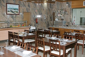 A restaurant with marble walls, multiple dining tables, and chairs. There is a bar area with bottles and glasses.