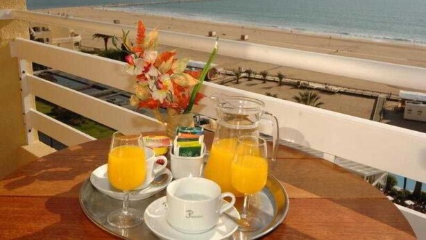 Desayuno con jugo de naranja y pastelería sobre una bandeja, con vista a la playa.