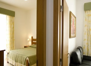 A bedroom with a bed, a nightstand, a lamp, a framed picture on the wall, and a sofa. - Hotel Santa Catarina Algarve (Portimão)