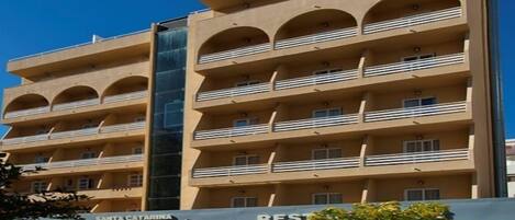 Un hotel de varios pisos con balcones, un ascensor de vidrio en el centro y un letrero que dice 'Hotel Santa Catalina'.
