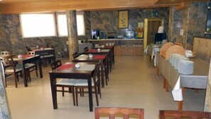 A dining area with multiple tables and chairs, a buffet setup, and a stone wall.