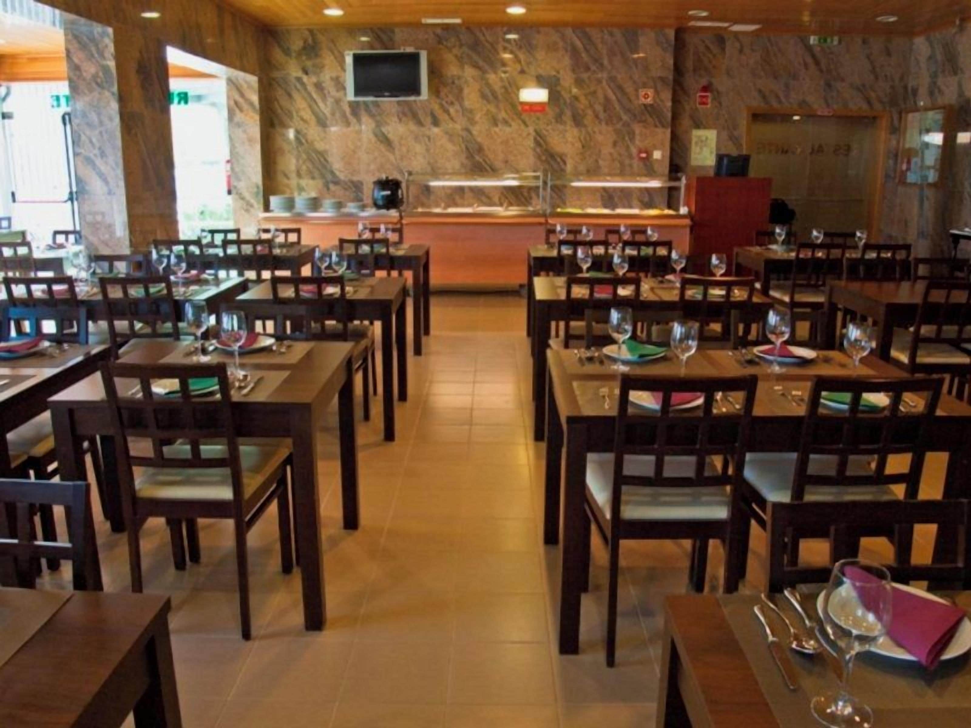 A restaurant with multiple tables and chairs, a marble wall, and a television mounted on the wall.
