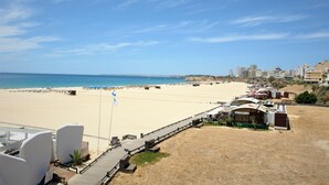 Een hotel aan het strand met een houten terras, ligbedden en parasols.
