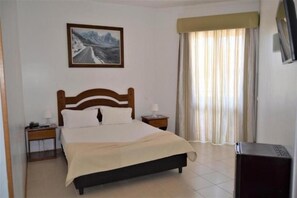 A hotel room with a bed, a nightstand, a TV, and a painting on the wall.