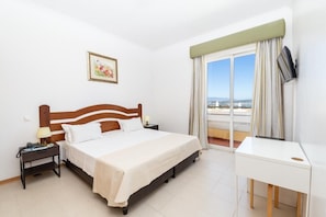 A hotel room with a bed, a desk, a nightstand, a TV, a window with curtains, and a painting on the wall. - Hotel Santa Catarina Algarve (Portimão)