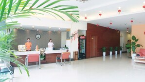 A hotel reception area with a reception desk, two receptionists, a Coca-Cola refrigerator, and a red sofa. - Ane Hotel - Eying Branch (Chengdu)
