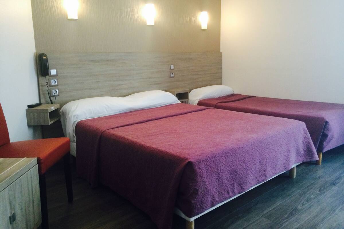 A hotel room with two beds, a wooden headboard, bedside tables with lamps, a telephone, and a red chair.