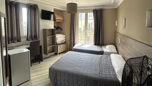 Ein Hotelzimmer mit zwei Betten, einem Schreibtisch, einem Stuhl, einem kleinen Tisch, einem Fernseher und einem Fenster mit Vorhängen.