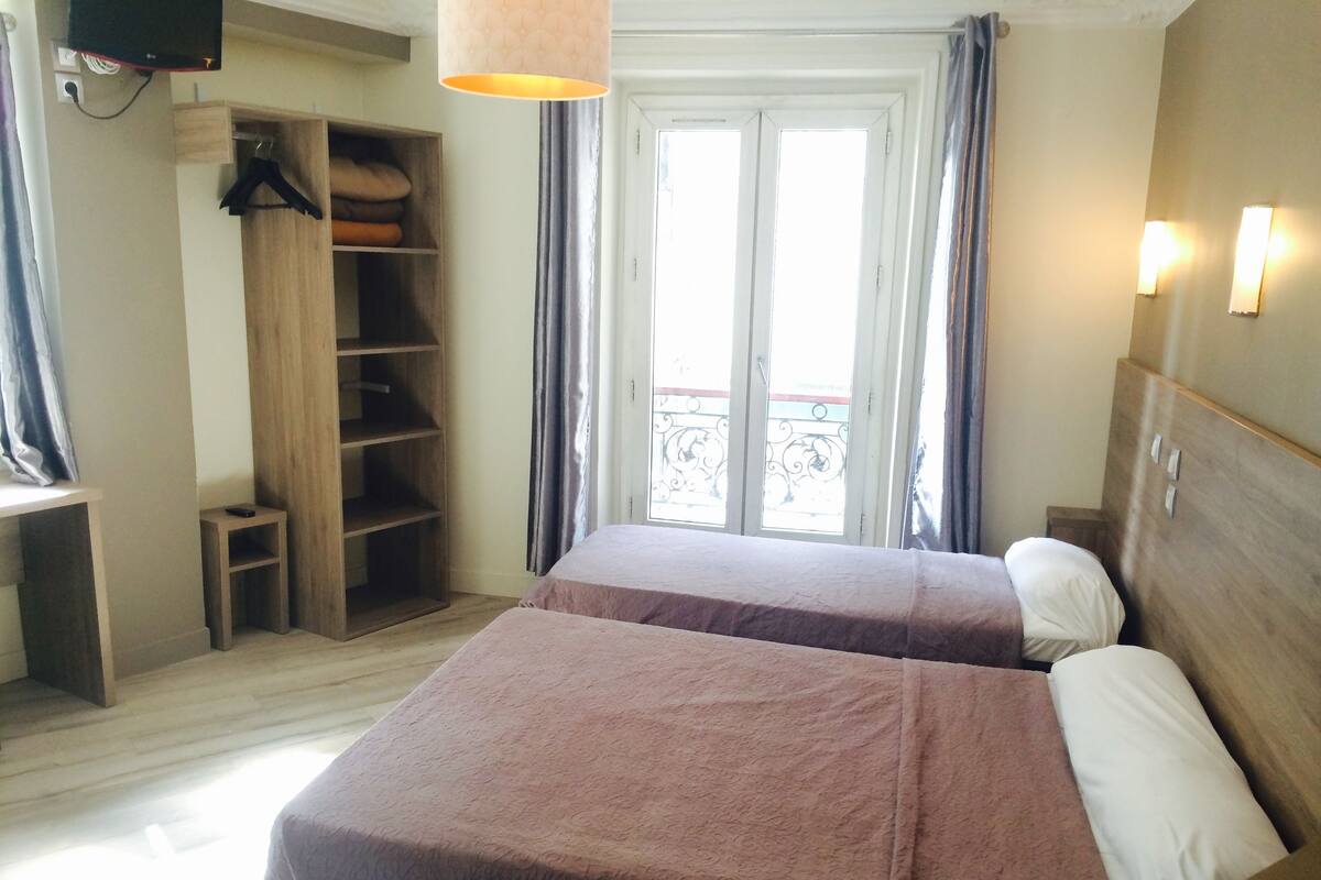 A hotel room with two beds, a wardrobe, a desk, and a balcony with a view.