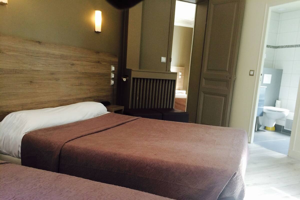 A hotel room with two beds, a wooden headboard, a nightstand, and a bathroom visible through an open door.