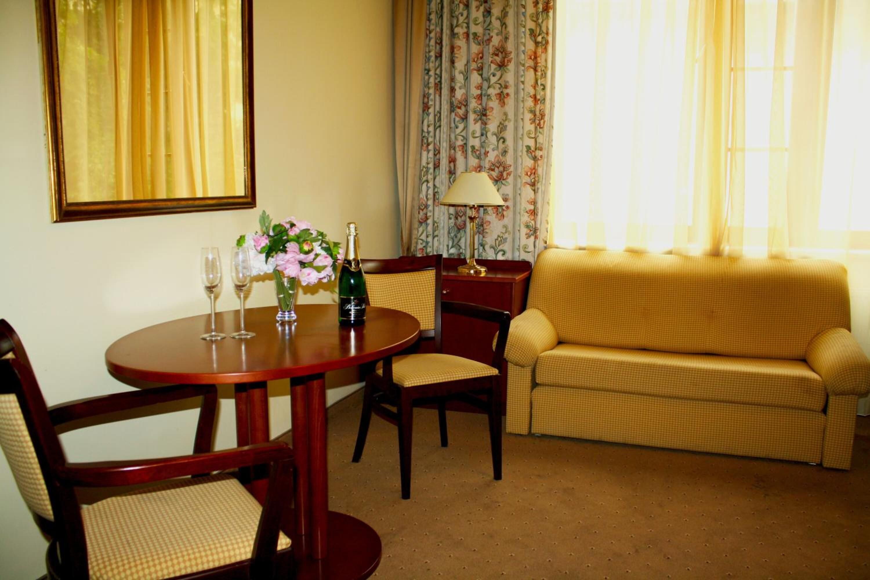 A dining area with a round table, two chairs, a sofa, and a lamp.