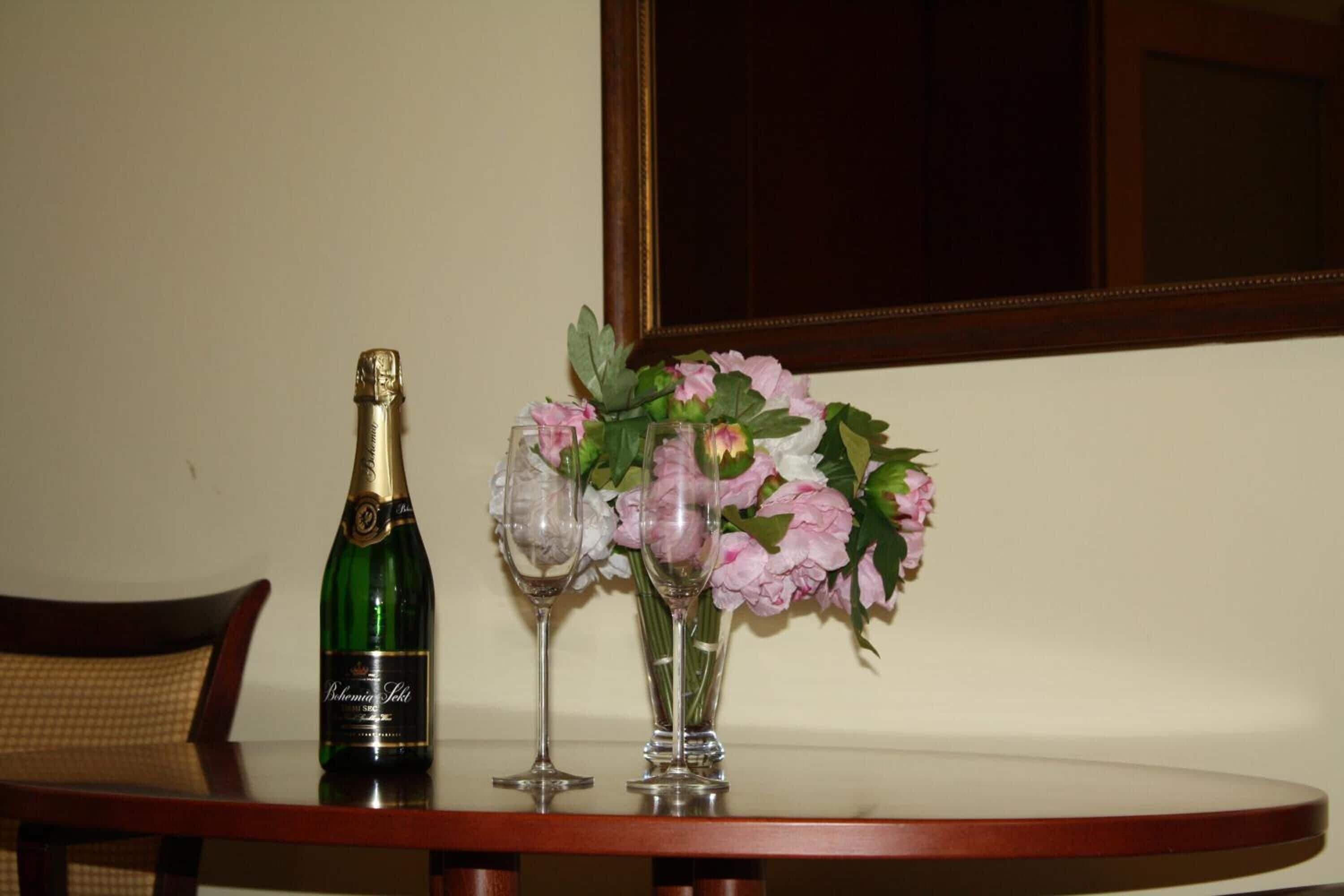 Eine Champagnerflasche, zwei Weingläser und eine Vase mit rosa Blumen auf einem Tisch.
