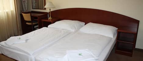 A double bed with white linens, a wooden headboard, a bedside table with a lamp, and a chair.