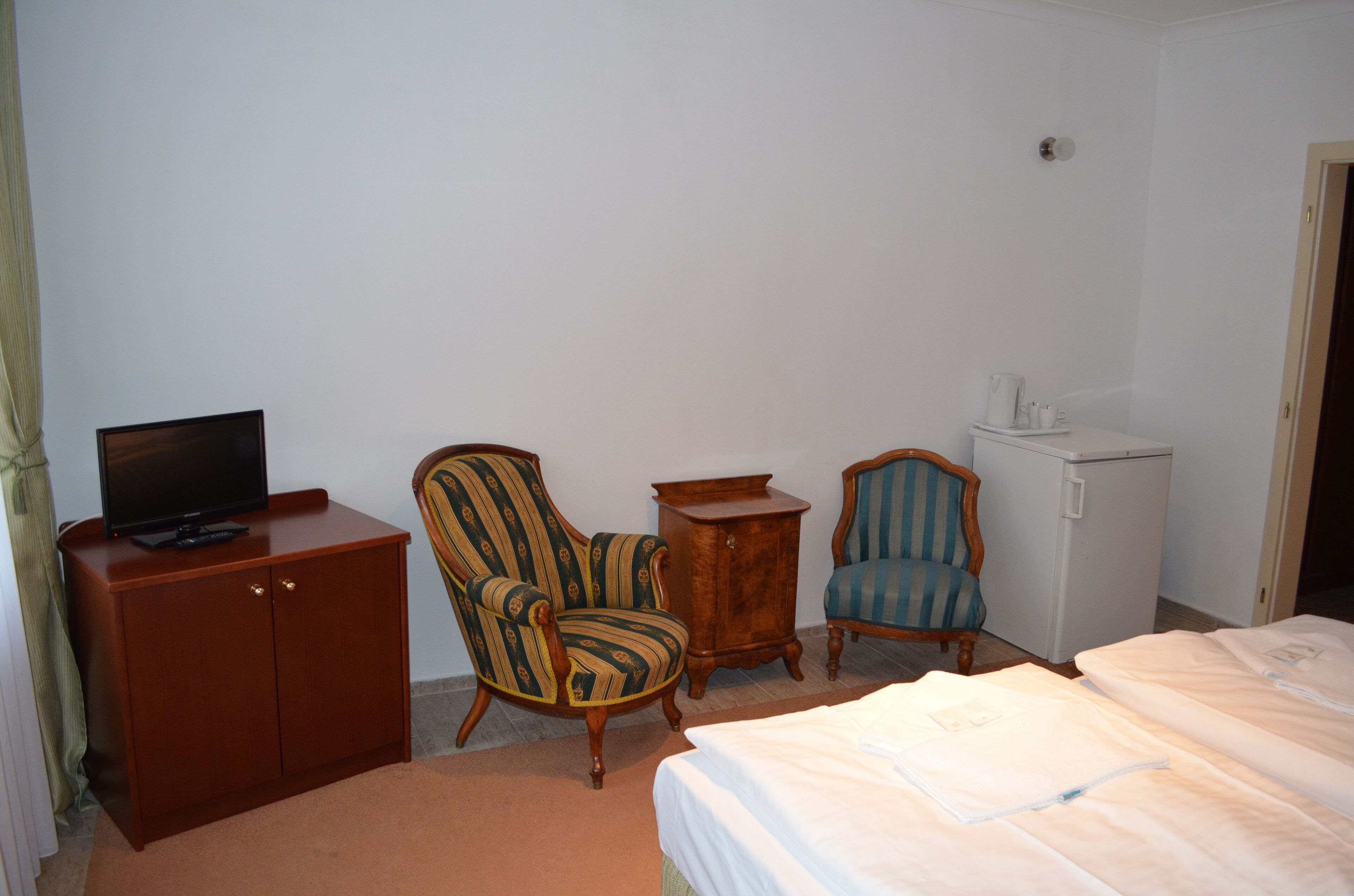 A hotel room with a bed, a television on a cabinet, two armchairs, and a small refrigerator.