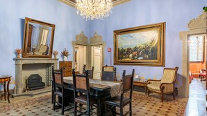 Una habitación con una mesa de comedor, sillas, una chimenea, una araña y un cuadro grande enmarcado.