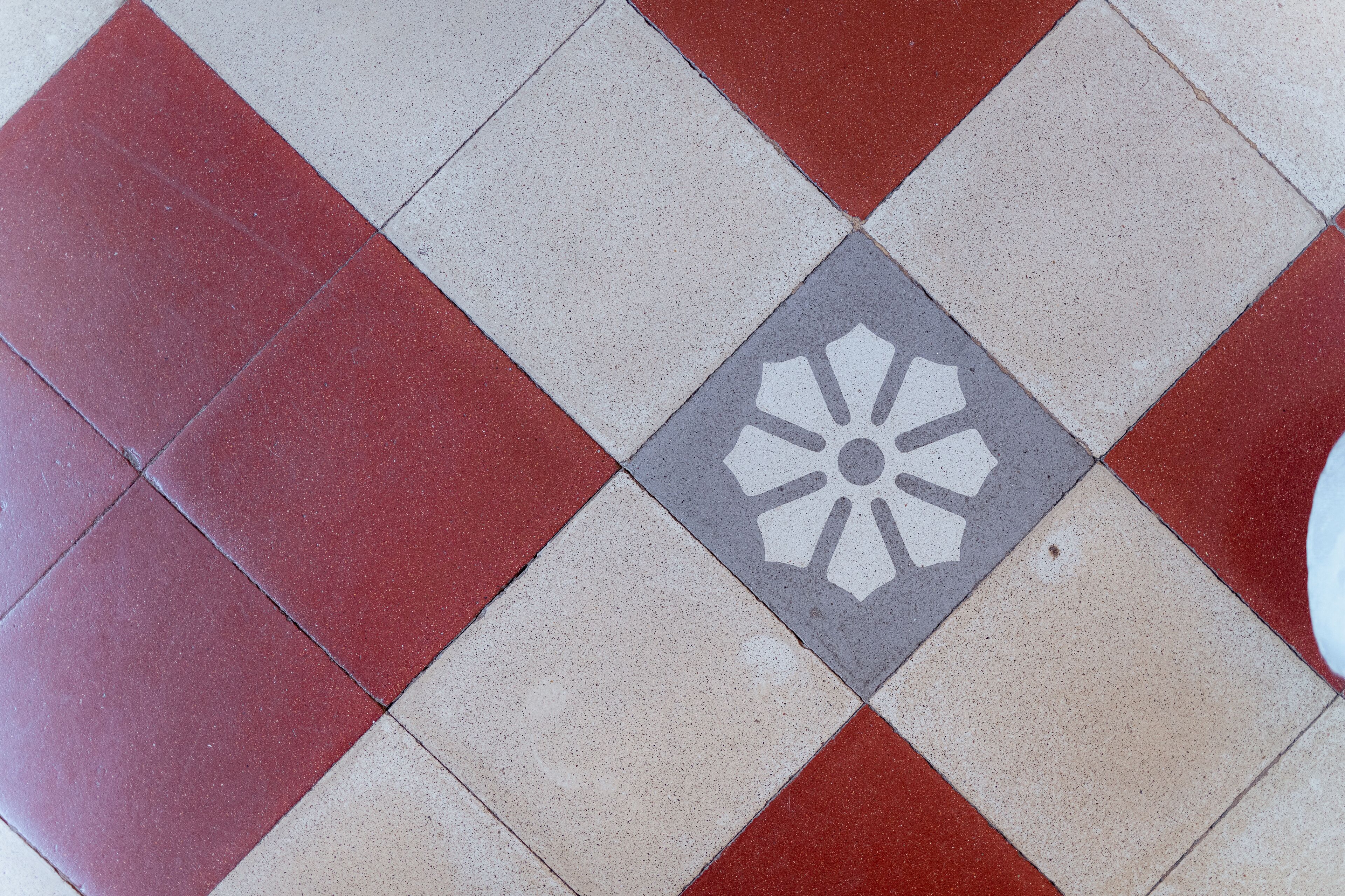 Un suelo con un diseño de baldosas rojas y blancas, y una baldosas central gris con un símbolo blanco.