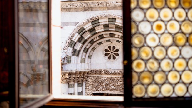Vista a través de una ventana con un arco de piedra y un muro decorado.