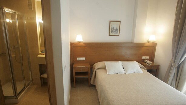 A hotel room with a bed, a nightstand, a lamp, a phone, and a shower area. - Hotel Goartín (Málaga)