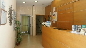 A hotel reception area with a wooden reception desk, a potted plant, and informational brochures. - Hotel Goartín (Málaga)