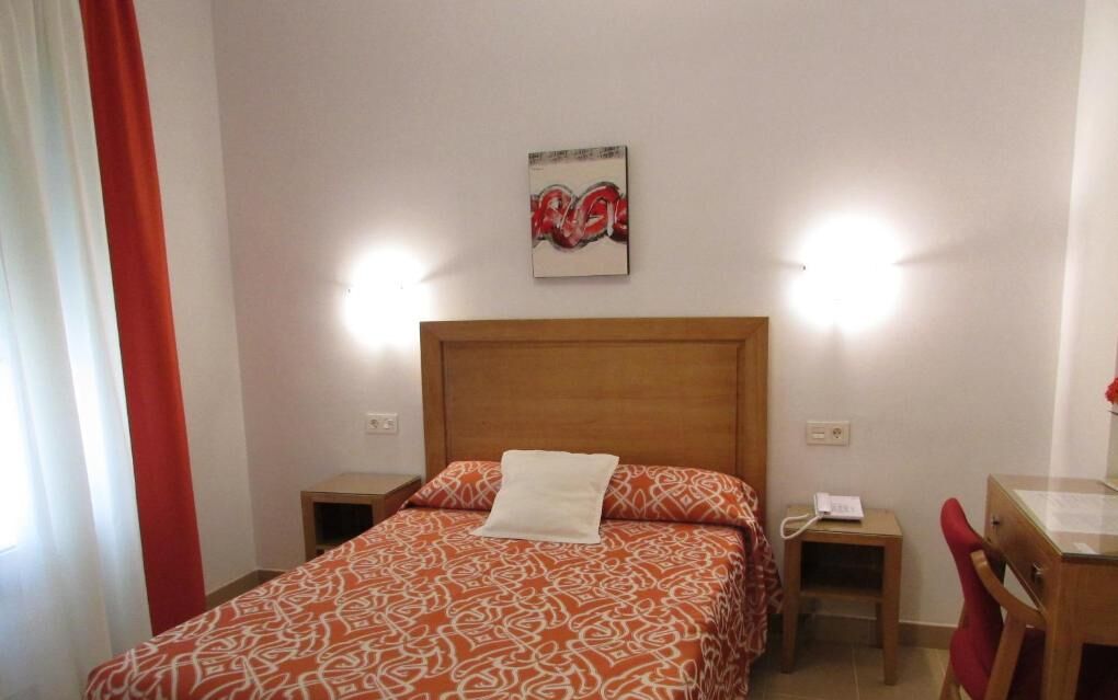 Een hotelkamer met een bed, nachtkastje, stoel en bureau.