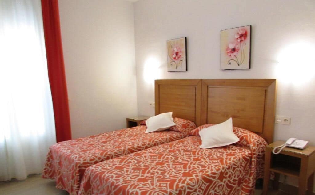 Una cama doble con ropa de cama estampada, un cabecero de madera, mesitas de noche con lámparas y dos cuadros florales en la pared.