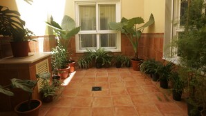 A sunlit hallway with terracotta tiles, a window with white frames, and various potted plants. - Hotel Goartín (Málaga)