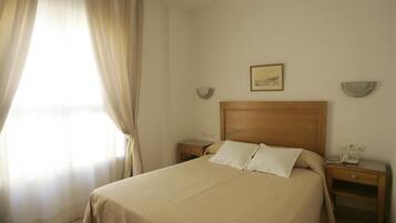 A hotel room with a bed, bedside tables, a nightstand, a lamp, and a window with curtains.