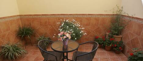 Un patio con una mesa redonda y cuatro sillas, rodeado de plantas y flores en macetas.