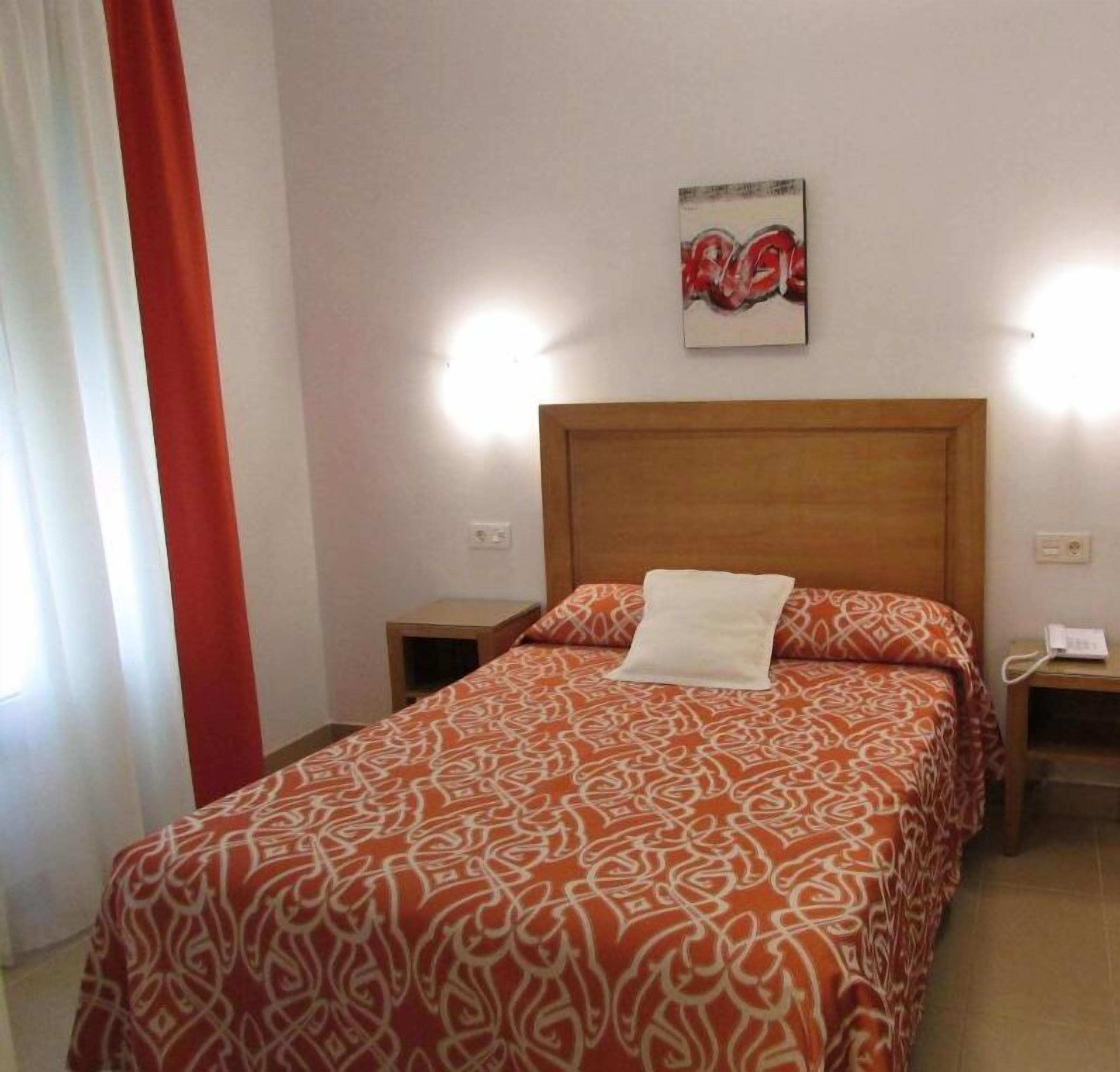 Una habitación de hotel con una cama, una mesita de noche, un teléfono en la pared y un cuadro.