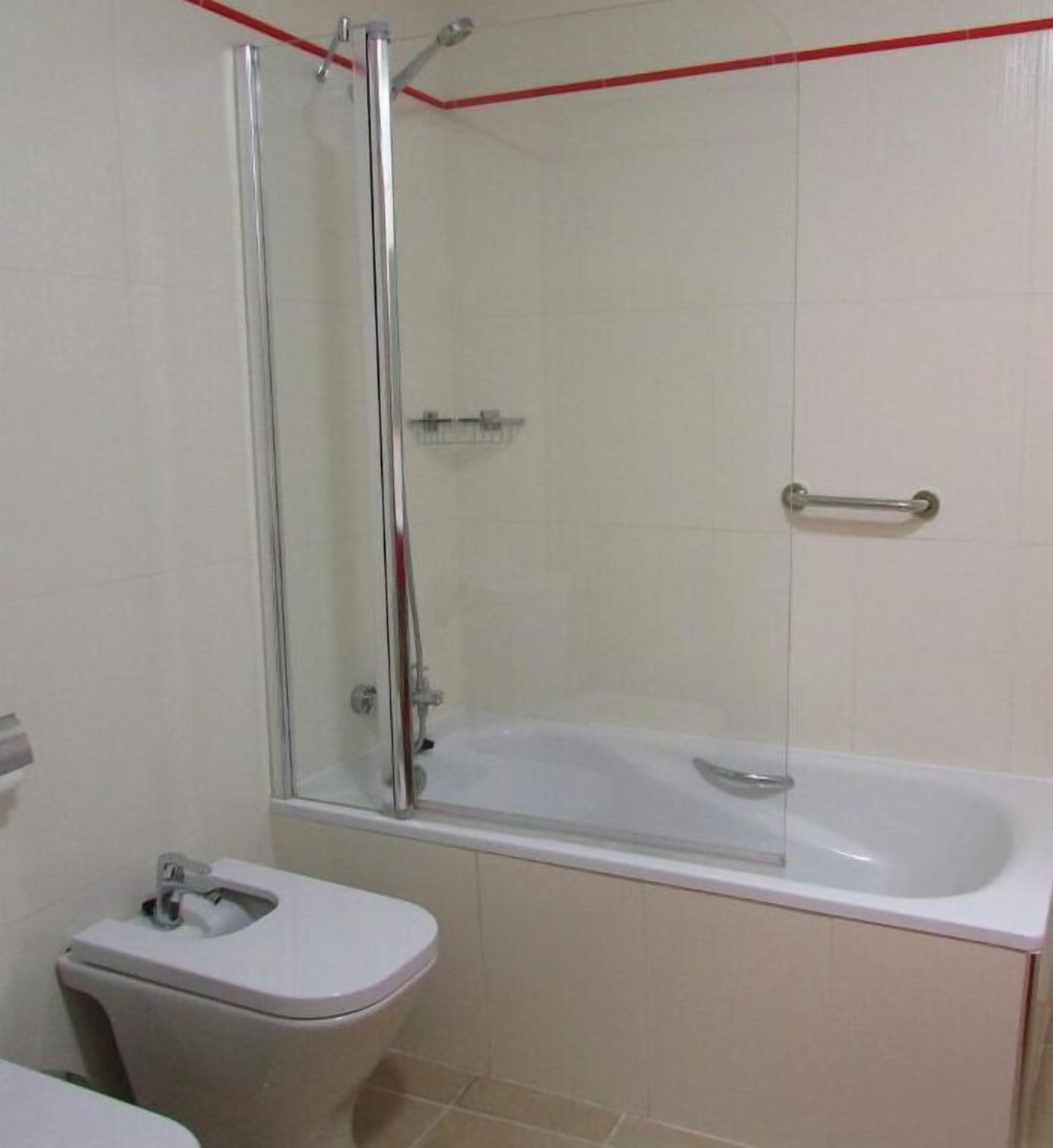 Een badkamer met een douche met glazen wand, een wit bad en een toilet.